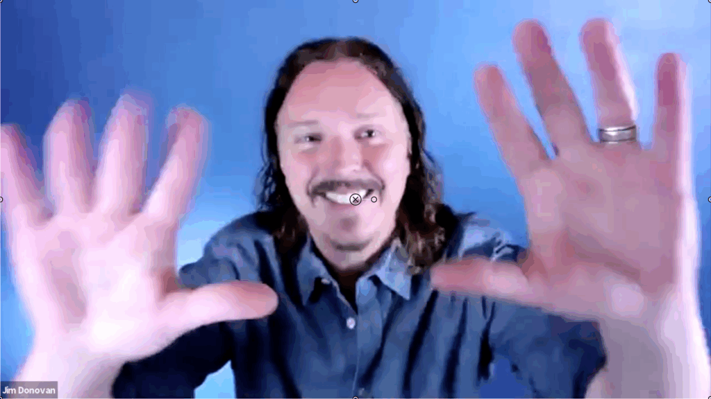 Jim Donovan waving hands at camera and smiling.